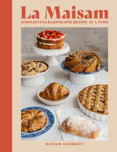 Book cover titled La Maisam with the subtitle Simplifying Baking One Recipe at a Time; shows an assortment of pastries (cakes, croissants, cookies, pies) arranged on a white table against a beige background.