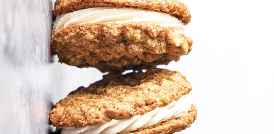 Chai Oatmeal Sandwich Cookies Golden-brown sandwich cookies with white cream filling stacked vertically along a wall surface