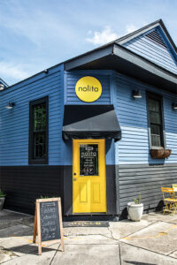 Blue storefront with bright yellow door and circular Nolita sign above the entrance.