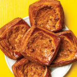 Plate of five golden, square savory pastries with a cheesy filling on a white plate against a bright yellow background.