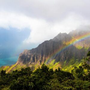 jake-houglum-dxdA7qd7Y9o-unsplash Coastal cliffs with green vegetation and a rainbow arcing over misty mountains by the sea.