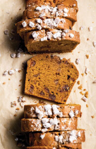 Sliced nutty loaf cake with walnuts and a light dusting of powdered sugar on parchment