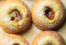 Pumpkin Cheesecake Brioche Buns Six powder-dusted pastries with jam centers arranged on a wooden surface, warm golden-brown and glossy in appearance.