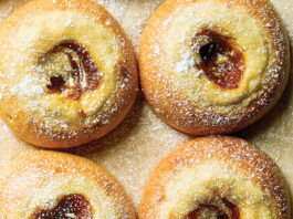Pumpkin Cheesecake Brioche Buns Six powder-dusted pastries with jam centers arranged on a wooden surface, warm golden-brown and glossy in appearance.