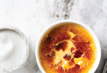 Pumpkin Crème Brûlée Two ramekins of crème brûlée with caramelized tops on a marble countertop, sugar bowl in the background.