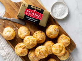 Gouda-and-Bacon Gougères Golden-brown pastry bites scattered on a wooden cutting board with a box of unsalted butter nearby and a measuring cup in the background (food scene)