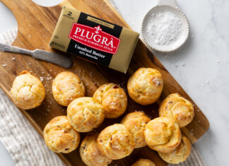 Gouda-and-Bacon Gougères Golden-brown pastry bites scattered on a wooden cutting board with a box of unsalted butter nearby and a measuring cup in the background (food scene)