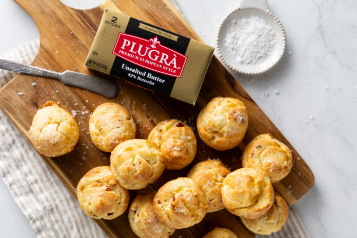 Golden-brown pastry bites scattered on a wooden cutting board with a box of unsalted butter nearby and a measuring cup in the background (food scene)