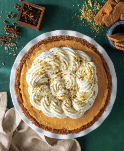 Pumpkin pie with piped whipped cream rosettes and a spiced crumb crust on a green table