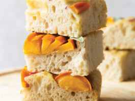 Sourdough Focaccia Stacked pieces of soft focaccia with apricot slices and fresh herbs on a wooden surface.