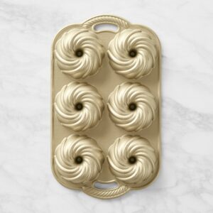 Gold silicone baking mold with multiple swirl-shaped pastry cavities arranged in a grid on a light marble surface